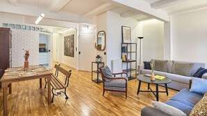 A spacious living area with a wooden floor, a sofa, a chair, a coffee table, and a dining table with placemats. - Magnificent Flat in Saint Germain des Pres (Paris)