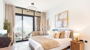 A modern bedroom with a large bed, a bedside table, a lamp, and a view of the outdoors. - Bloomfields VistaVibe STU Al Maryah  (Abu Dhabi)