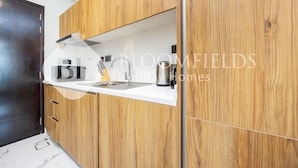 A modern kitchen with wooden cabinetry, a white countertop, and a stainless steel sink. - Bloomfields VistaVibe STU Al Maryah  (Abu Dhabi)