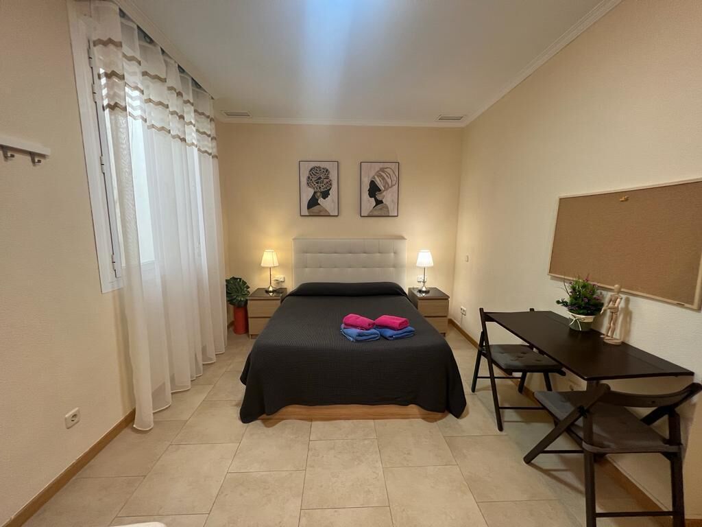 A bedroom with a bed, bedside tables with lamps, a desk, and two wall-mounted artworks.