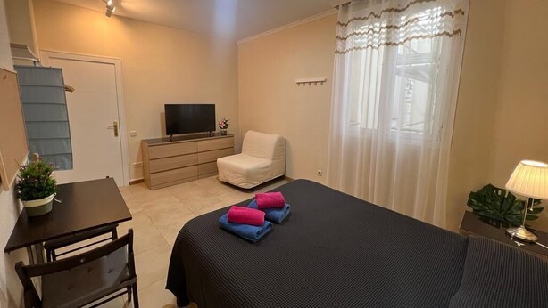 Habitación de hotel con cama, escritorio, silla, televisión y ventana con cortinas.