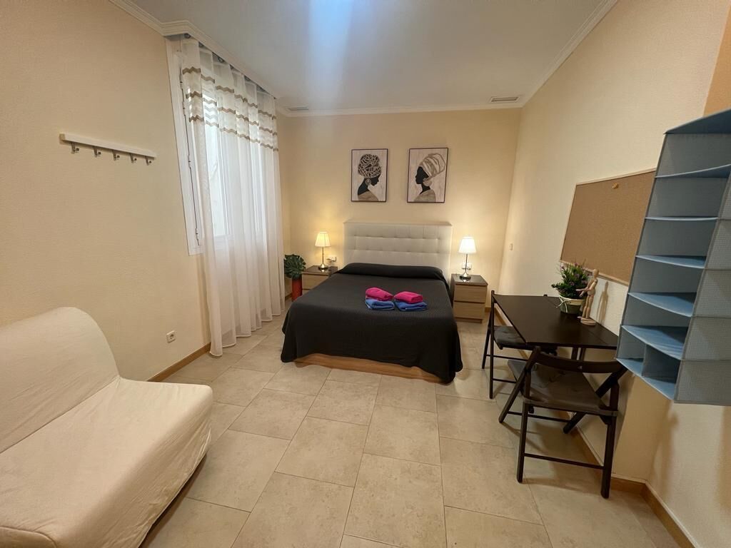 Un dormitorio con cama, escritorio, silla, sofá y estantería.