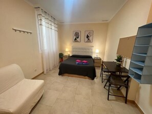 Ein Schlafzimmer mit einem Bett, einem Schreibtisch, einem Stuhl, einer Couch und einem Bücherregal.