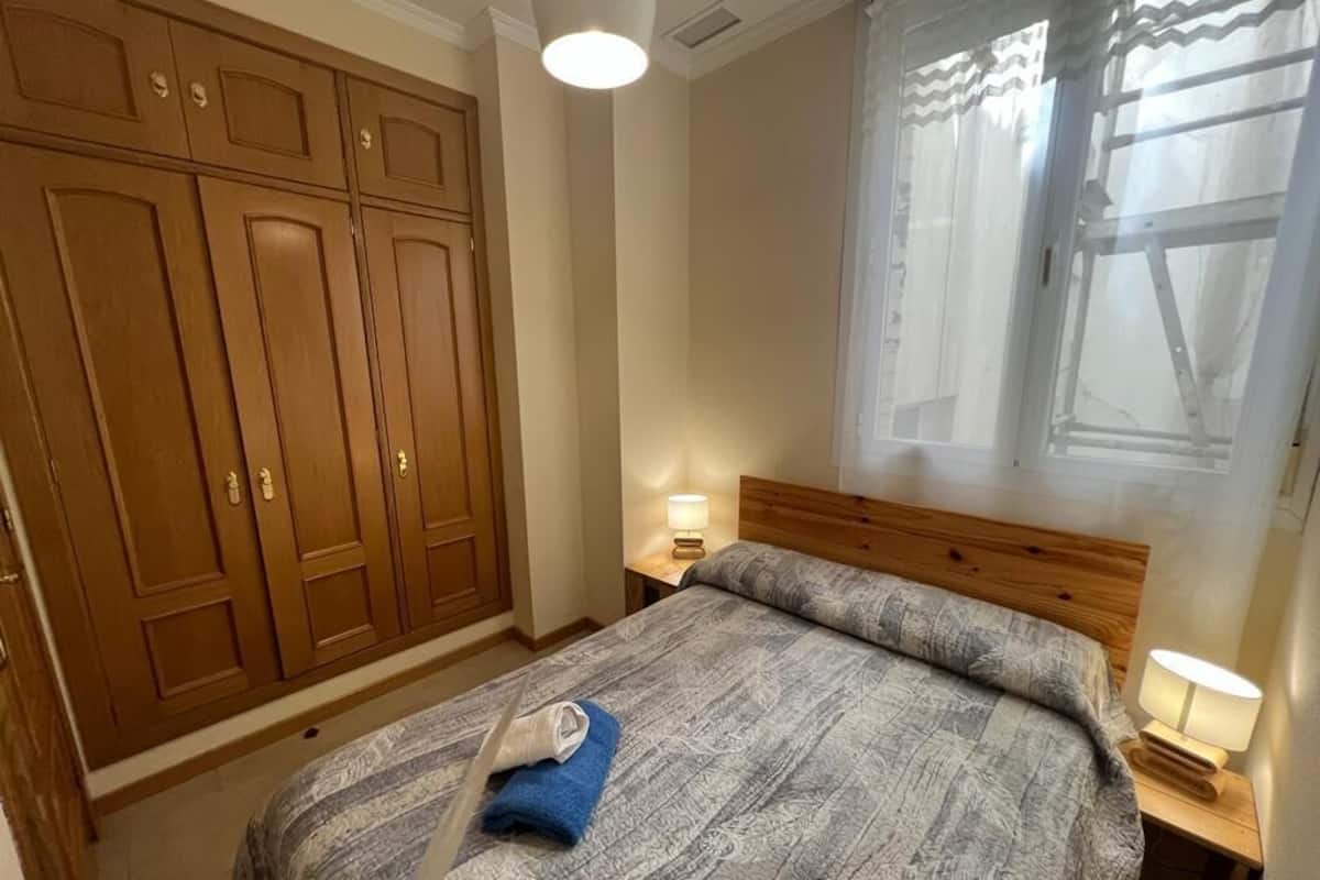 A bedroom with a large bed, wooden wardrobe, two bedside lamps, and a window with curtains.