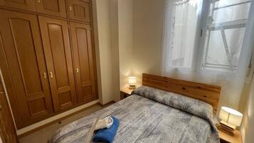 Un dormitorio con una cama grande, un armario de madera, dos lámparas de noche y un ventanal con cortinas.