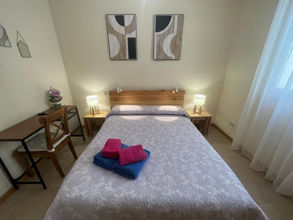 Een keurig opgemaakte slaapkamer met een bed, twee nachtkastjes, een bureau en stoelen.