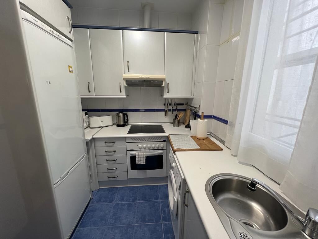 A compact kitchen with white cabinets, a sink, a stove, and a washing machine.