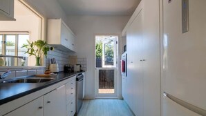 A narrow kitchen with white cabinets, a black countertop, and a window.