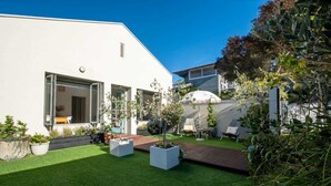 A modern house with a white exterior, a well-maintained lawn, and a patio area with seating.