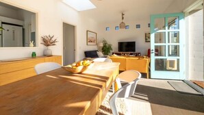 A dining area with a wooden table, chairs, a bowl of fruit, a television, and a door with glass panels.