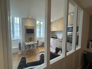 A modern kitchen with a built-in oven and microwave, a dining area with a table and chairs, and a large window providing natural light. - Cosy T1 bis completely renovated downtown (La Rochelle)