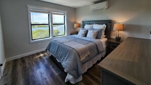 Une chambre à coucher avec un lit, deux tables de chevet avec des lampes, une fenêtre avec des stores et un climatiseur fixé au mur.