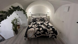 Une chambre à coucher avec un lit, une table de chevet, une lampe fixée au mur et une plante en pot.