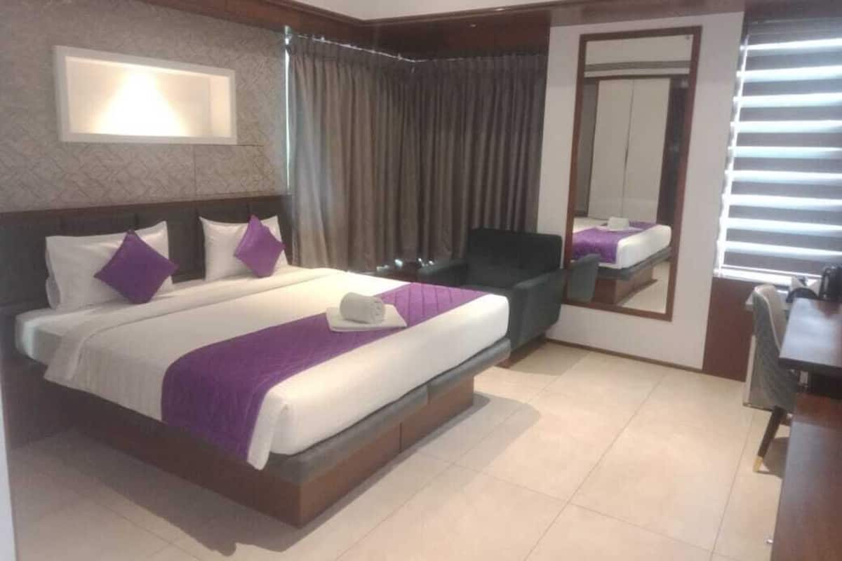 A hotel room with a large bed, a desk, a chair, and a mirror.