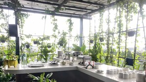 A modern kitchen with a view of the city, featuring hanging plants, a counter with dishes, and a large window. - SRS Suite (Bengaluru)