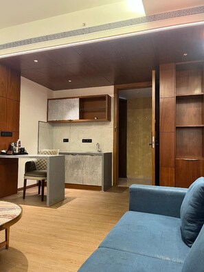 A modern living room with a blue sofa, a dining area with a table and chairs, and a kitchen with a built-in island and cabinets. - SRS Suite (Bengaluru)