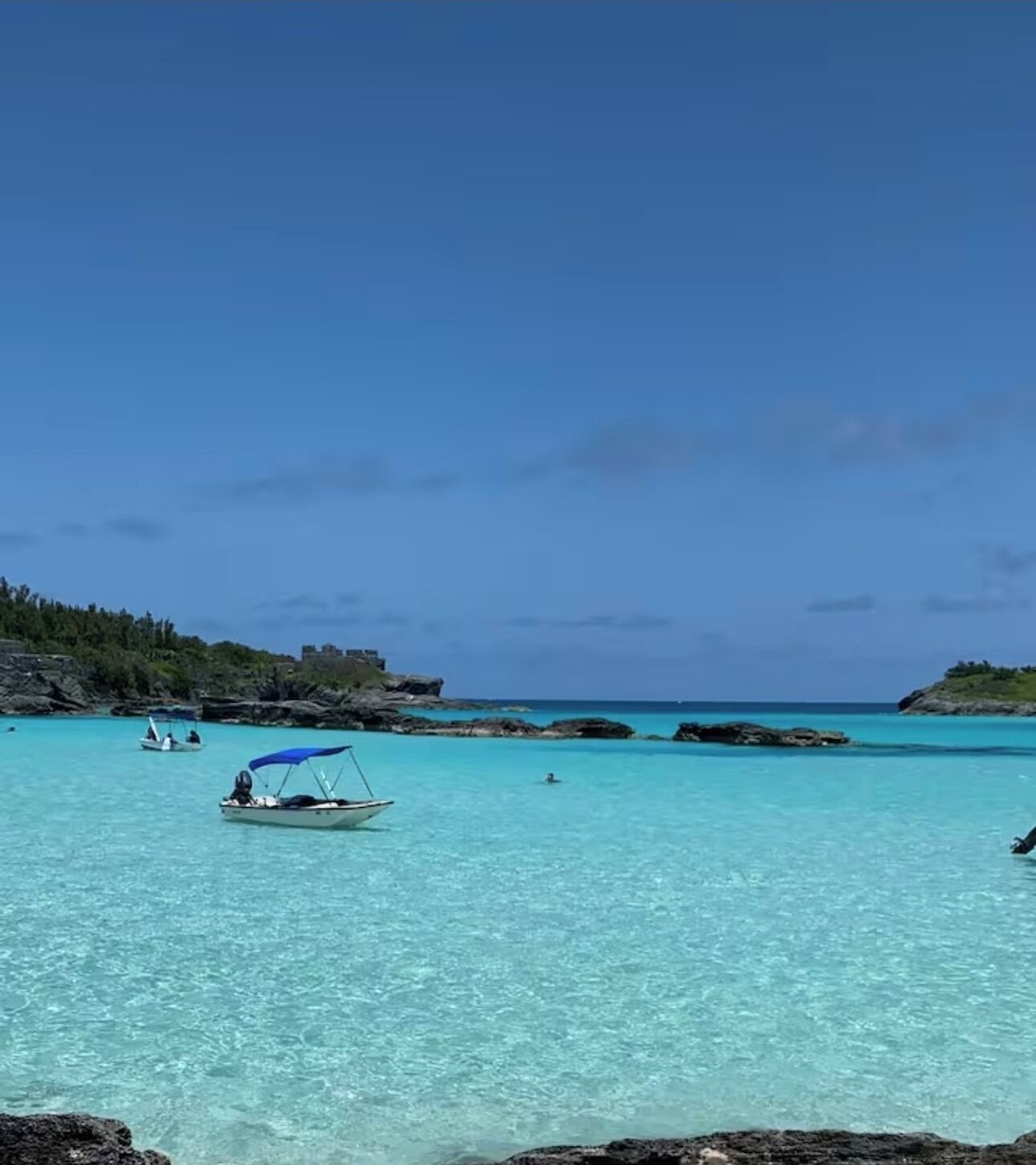 Een kustgezicht met helder turquoise water, rotsachtige rotsformaties en een boot met een blauw zonnedak.