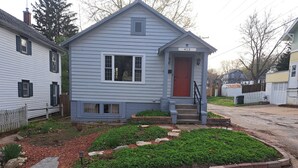 A two-story house with a red door, a front porch, and a small garden area with stepping stones. - Charming 2-bedroom cottage with WiFi, AC in enjoyable Fort Madison (Fort Madison)