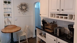 A kitchen with white cabinets, a wooden table, and a chair. There is a wreath on the wall and a basket of utensils on the counter. - Charming 2-bedroom cottage with WiFi, AC in enjoyable Fort Madison (Fort Madison)