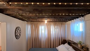 A bedroom with a bed, curtains, a clock, and string lights. - Charming 2-bedroom cottage with WiFi, AC in enjoyable Fort Madison (Fort Madison)