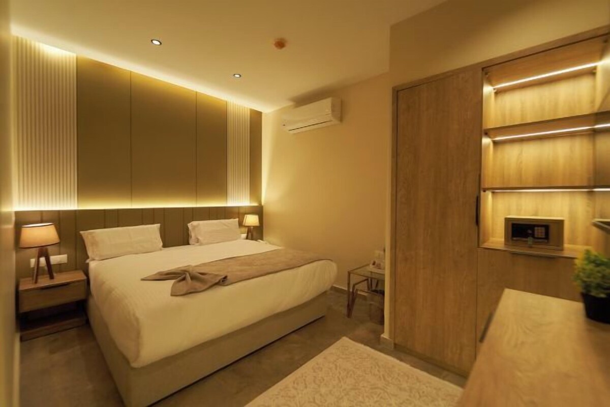A modern hotel room with a large bed, bedside tables, an air conditioning unit, and a wooden wardrobe.