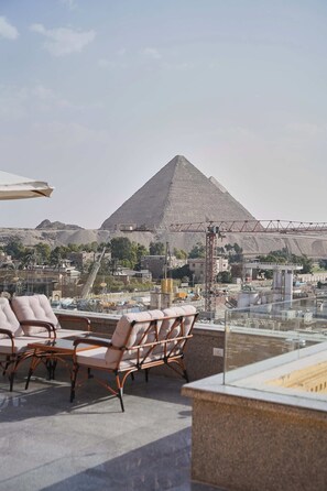 A rooftop terrace with lounge chairs and a view of a pyramid in the background. - Pyramids Secret Hotel (Giza)