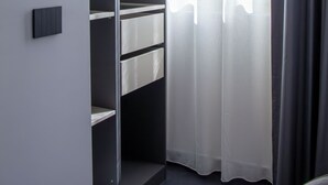 Ein moderner Kleiderschrank mit offenen Regalen und Kleiderstange, eine Schiebetür und ein Fenster mit transparenten Vorhängen.