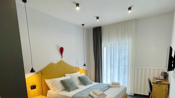 Ein modernes Hotelzimmer mit einem großen Bett, Nachttischen, einem Schreibtisch und einem Fernseher.