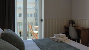 Ein Hotelzimmer mit Bett, Schreibtisch mit Stuhl, einem Balkon mit Sitzgelegenheit und Blick auf ein Gebäude.