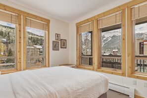 A bedroom with a bed, wooden windows, and a view of a mountainous landscape. - Tx204 Taylors Crossing 3 Bedroom Condo (Copper Mountain)