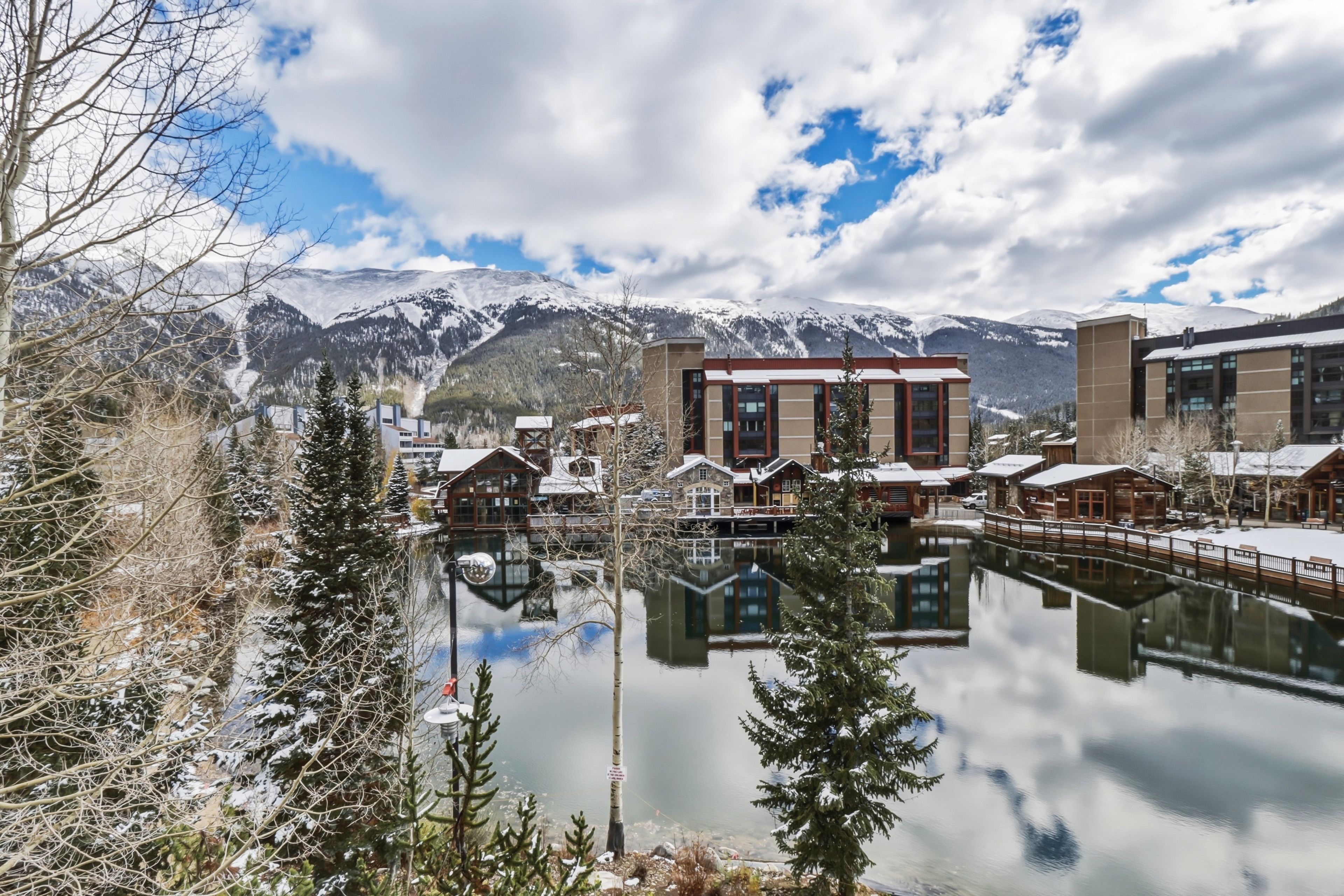 A lakeside hotel with reflection, snow-covered mountains, and modern buildings.