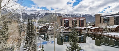 A lakeside hotel with reflection, snow-covered mountains, and modern buildings.