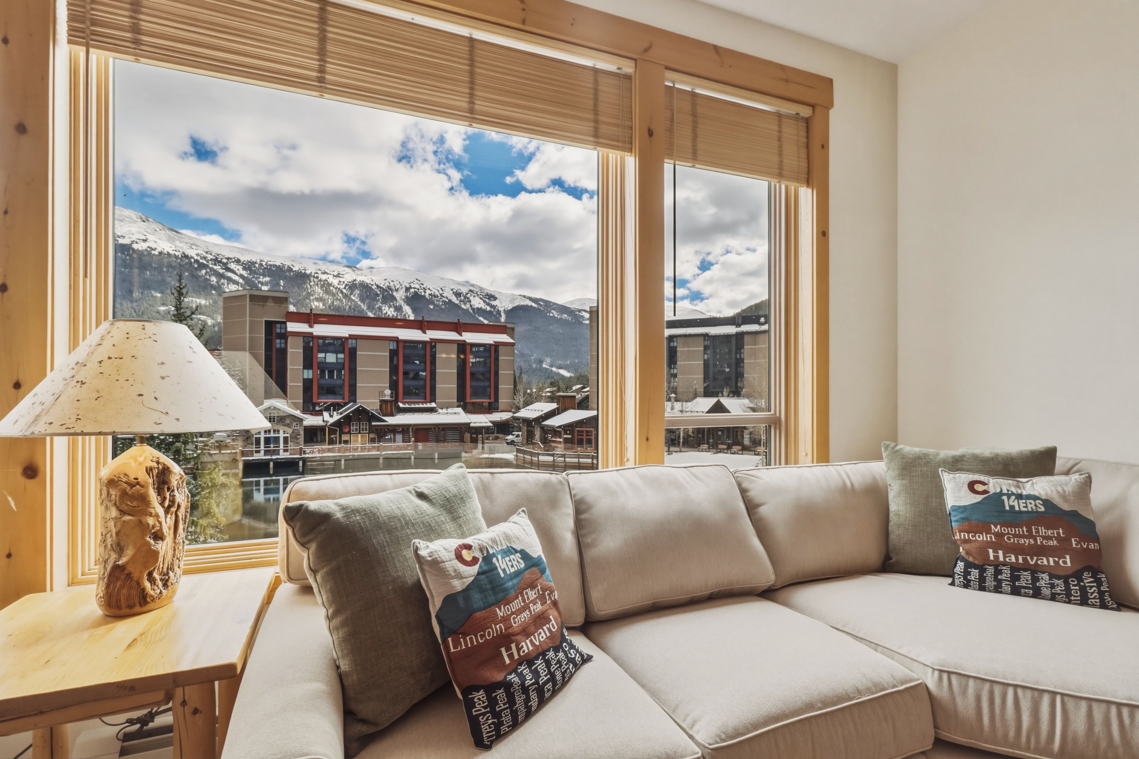 A modern living room with a sofa, lamps, and a view of a mountain resort.