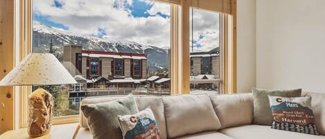A modern living room with a sofa, lamps, and a view of a mountain resort.