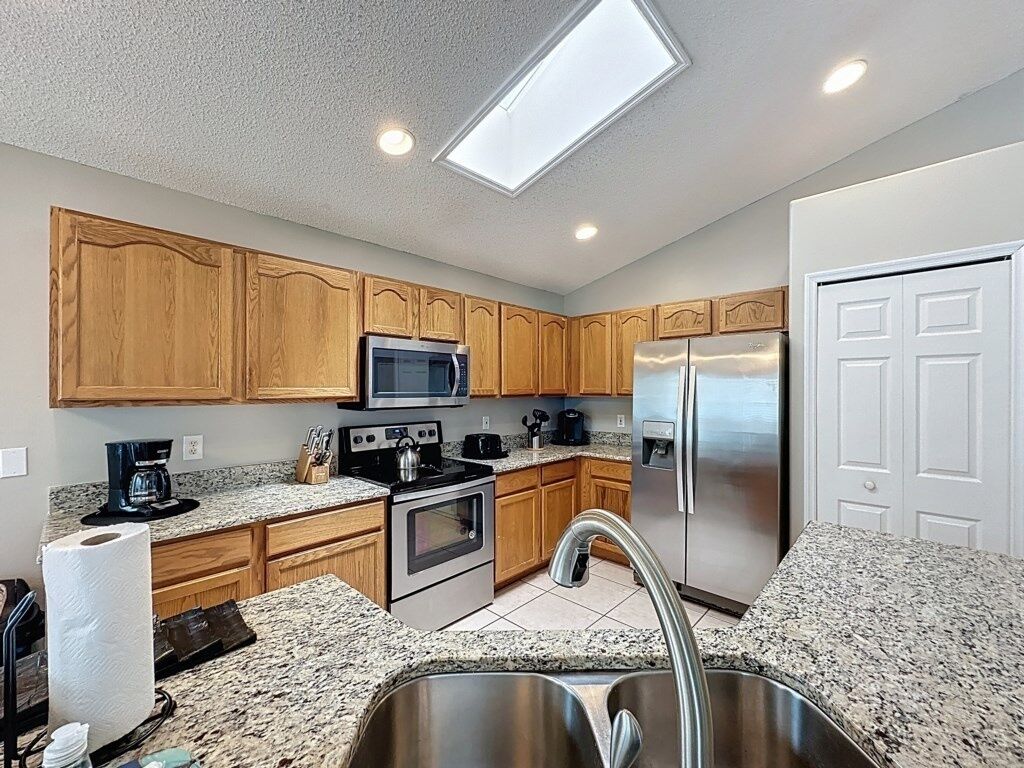 A modern kitchen with wooden cabinets, stainless steel appliances, granite countertops, and a skylight.