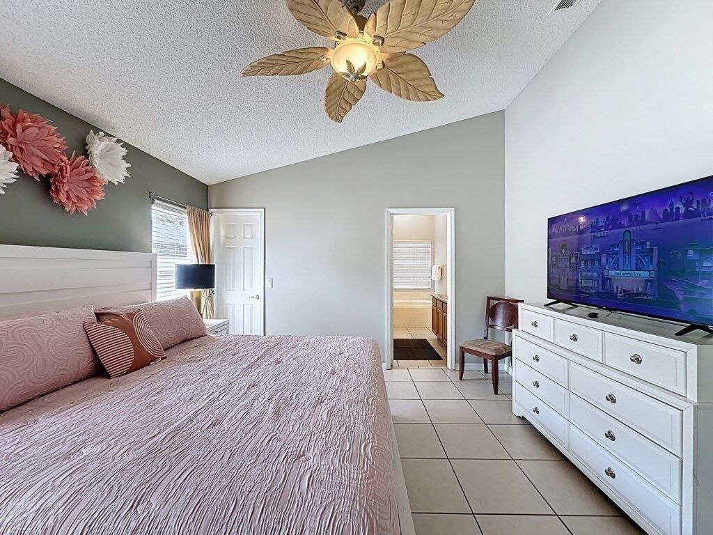 Une chambre à coucher avec un lit, un ventilateur de plafond, une télévision et une commode.