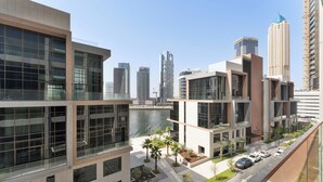 A modern building with large windows, a parking area, and a view of the city skyline. - Peninsula Five (Dubai)