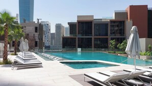 A rooftop pool area with lounge chairs and umbrellas, surrounded by modern buildings and palm trees. - Peninsula Five (Dubai)