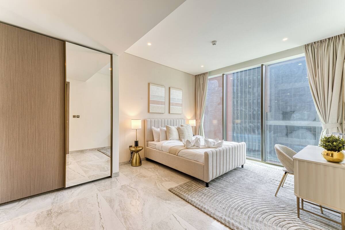 A modern bedroom with a large bed, a bedside table, a chair, and a large window.