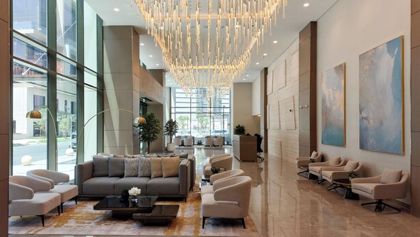 A spacious lobby with a modern chandelier, seating area, and large windows offering views of the street. - Peninsula Five (Dubai)