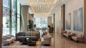 A spacious lobby with a modern chandelier, seating area, and large windows offering views of the street. - Peninsula Five (Dubai)