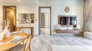 A modern living room with a large TV, a dining area with a wooden table and chairs, and a hallway leading to another room. - Peninsula Five (Dubai)