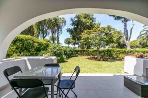 An outdoor patio with a table and chairs, surrounded by a white archway, overlooking a well-maintained garden with various trees and shrubs. - Holiday Home 'Miraflores Resort Luxury' with Sea View, Wi-Fi and Air Conditioning (Mijas)