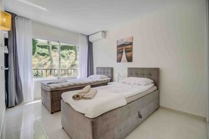 A bedroom with two beds, a large window with curtains, a painting on the wall, and a ceiling fan. - Holiday Home 'Miraflores Resort Luxury' with Sea View, Wi-Fi and Air Conditioning (Mijas)