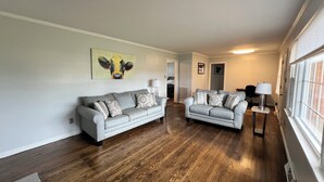 Un salon avec deux canapés gris, un plancher en bois et un tableau accroché au mur.
