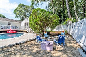 Un patio trasero con piscina, un árbol grande y mobiliario exterior.