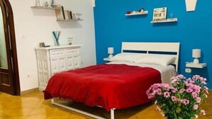 A bedroom with a bed, a nightstand, a bedside table, a vase with flowers, and a blue wall. - MAISON SOSò NAPLES vacation home Entire apartment in the center of Naples (Napoli)