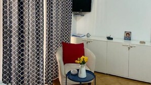A modern room with a white sofa, a small round table with a vase of flowers, and a TV mounted on the wall. - MAISON SOSò NAPLES vacation home Entire apartment in the center of Naples (Napoli)
