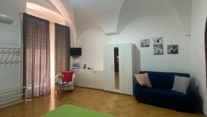 A spacious living room with a green sofa, a blue sofa, and a small table with a red cushion. There is a white wardrobe and a door leading to another room. - MAISON SOSò NAPLES vacation home Entire apartment in the center of Naples (Napoli)