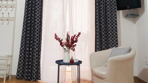 A living room with a white armchair, a small table with a vase of flowers, and a television mounted on the wall. - MAISON SOSò NAPLES vacation home Entire apartment in the center of Naples (Napoli)